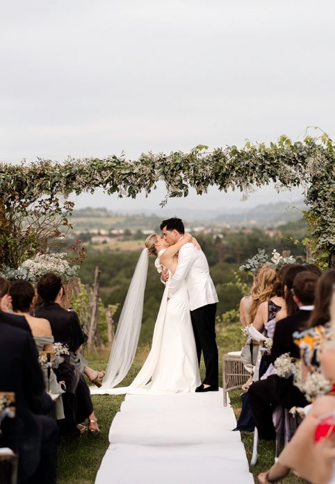 Il bacio degli sposi sotto l’arco di fiori con le colline sullo sfondo